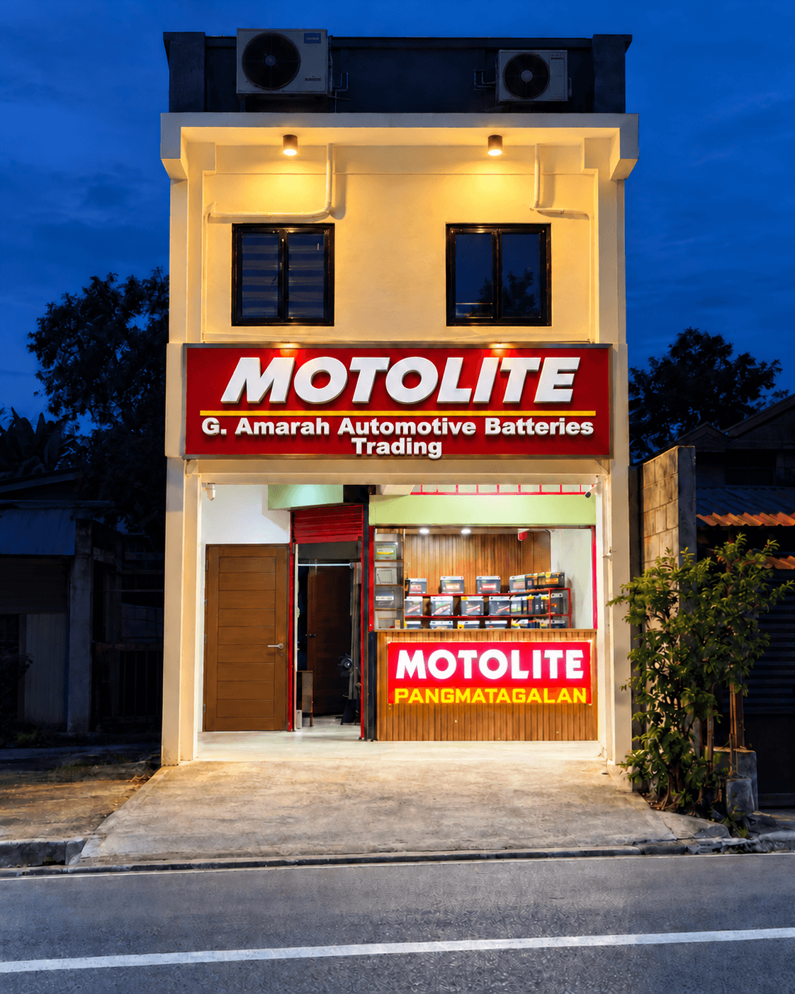 G. Amarah Automotive Batteries Trading storefront with illuminated Motolite signage at dusk